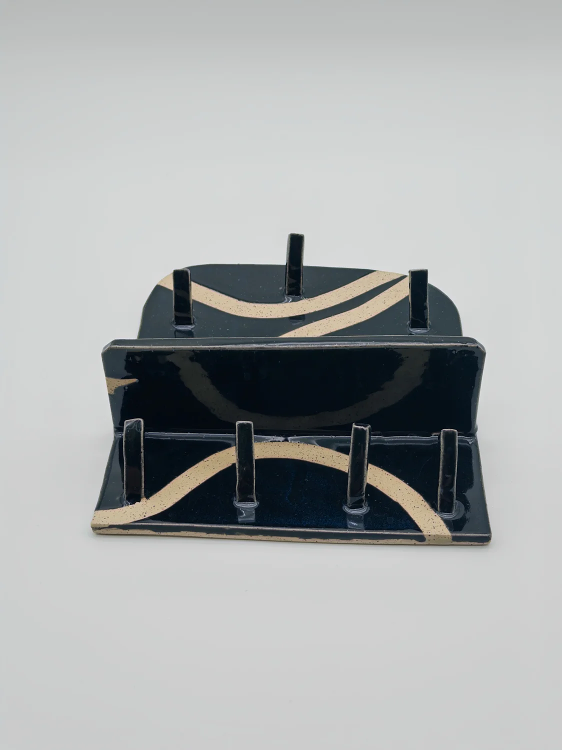 Black rectangular ceramic stand with cream curved stripes and upright pegs