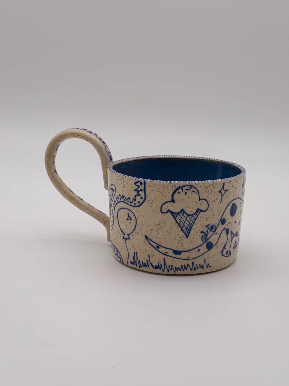 Cream mug with blue doodles, a blue interior, and a curved handle