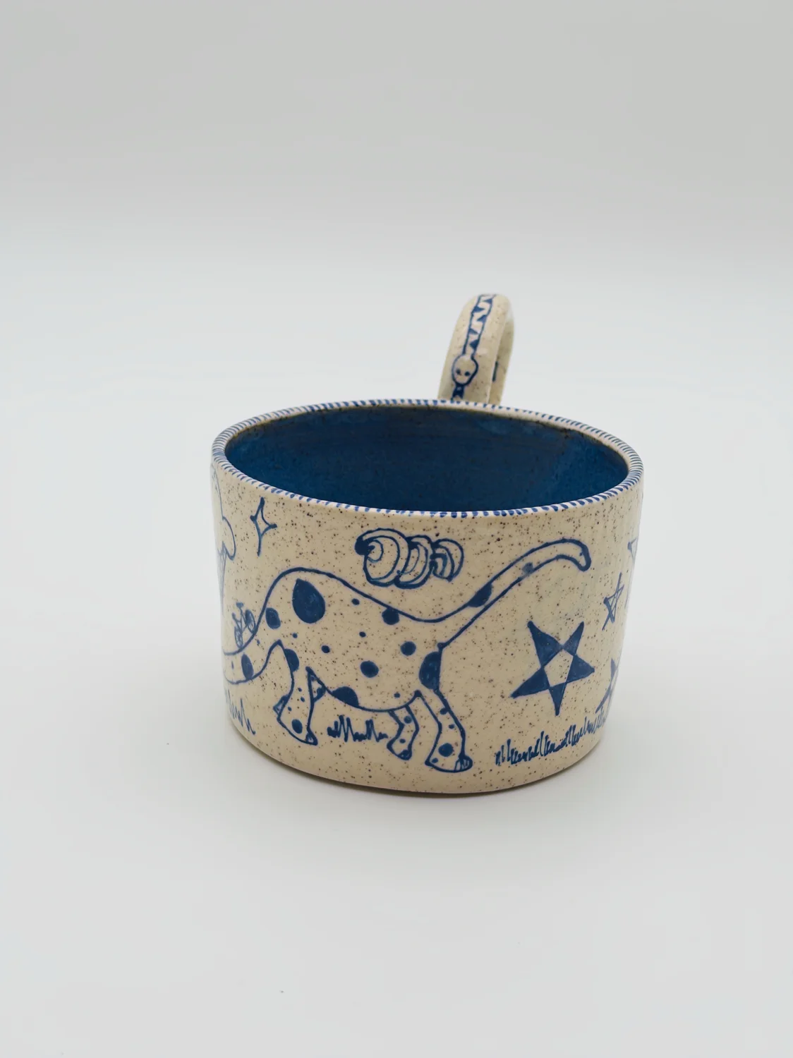 Cream mug with blue doodles, a blue interior, and a curved handle, view 3