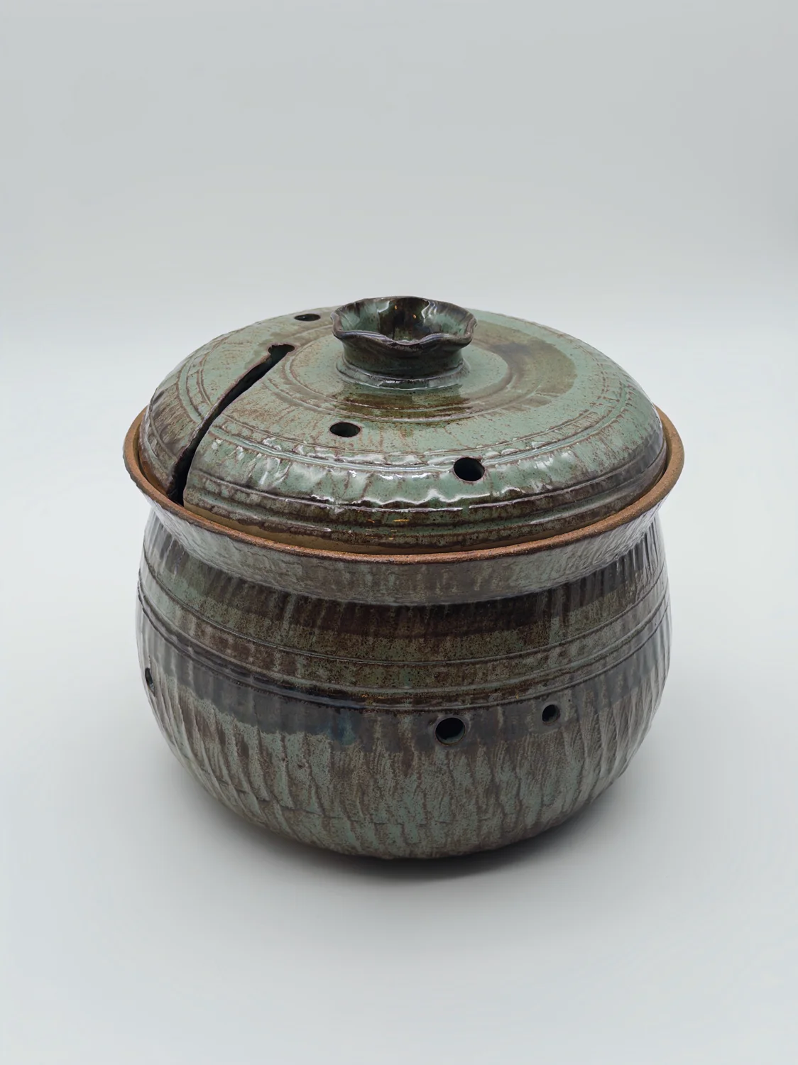Brown and green lidded pot with small holes and a notch in the lid